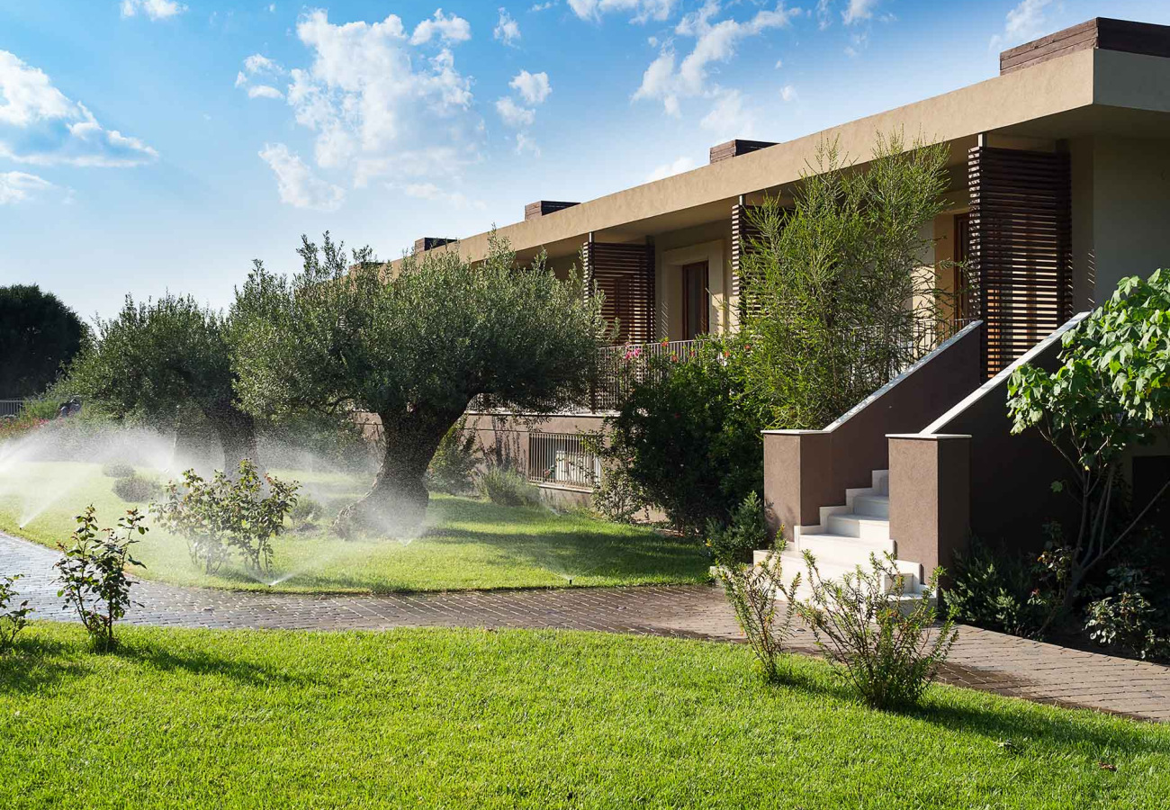 Giardino curato con irrigazione, alberi e moderno edificio sotto un cielo sereno.