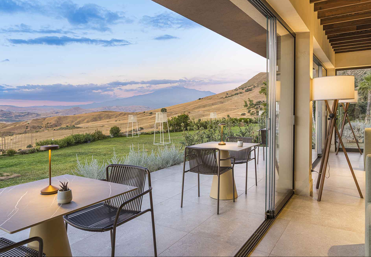 Terrazza moderna con vista panoramica su colline, arredi eleganti e lampade da tavolo.