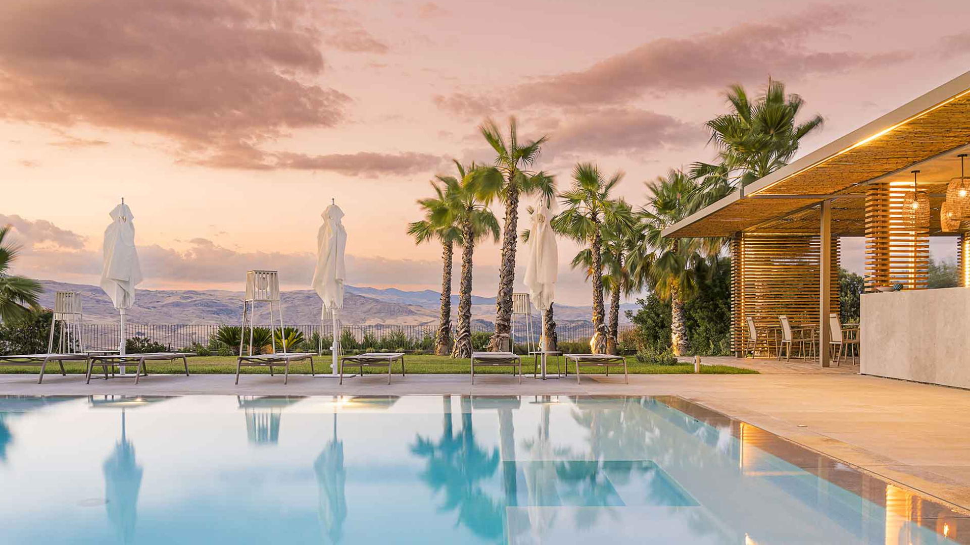 Piscina elegante al tramonto, con palme e area lounge moderna.